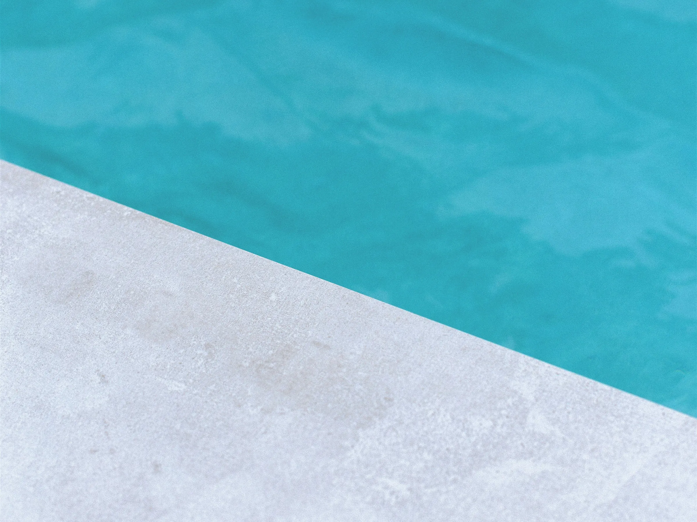 Stock photo: the edge of a pale concrete pool deck meeting turquoise pool water