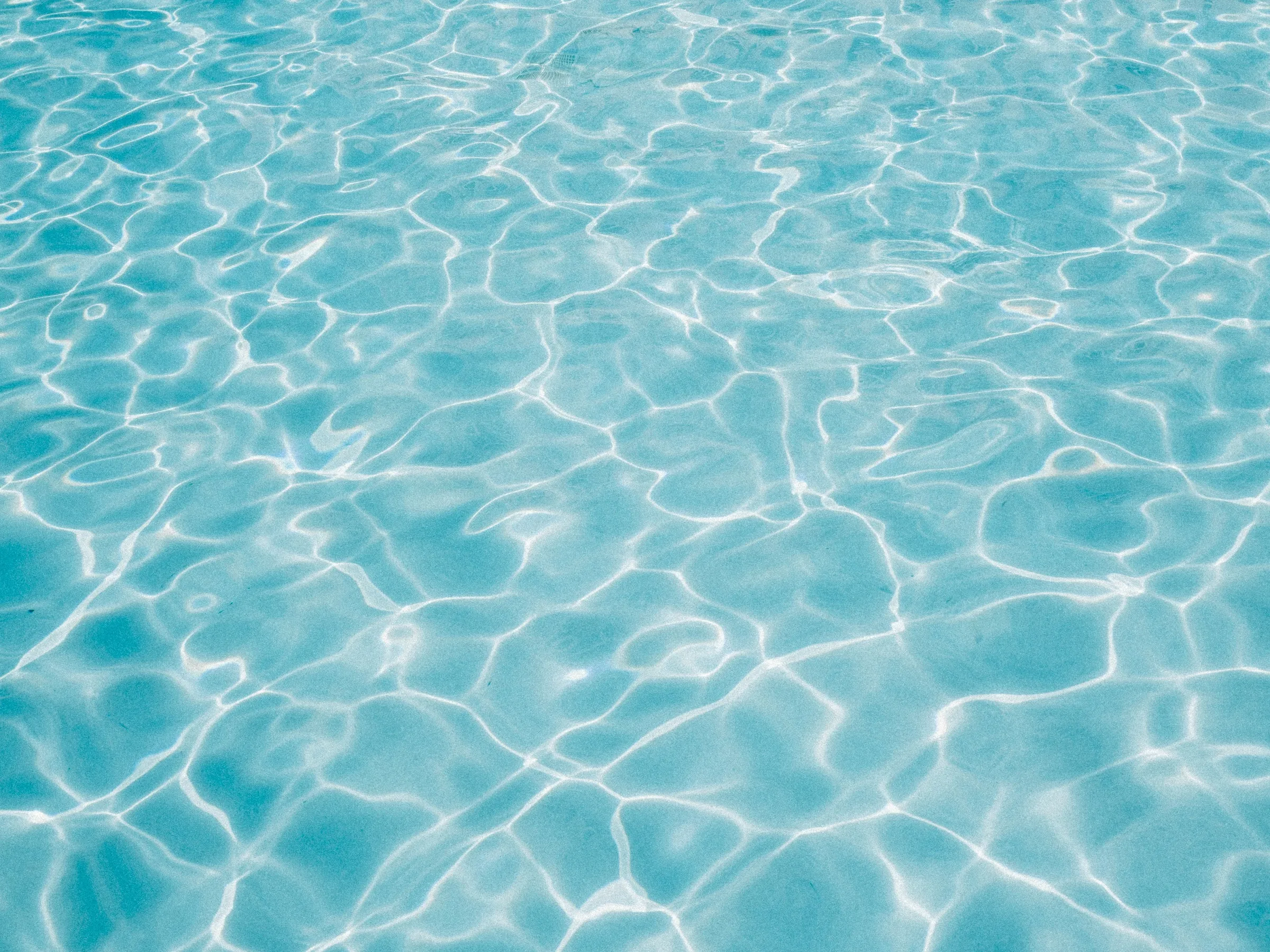 Stock photo: sunlight rippling across clear blue water over a pale pool floor